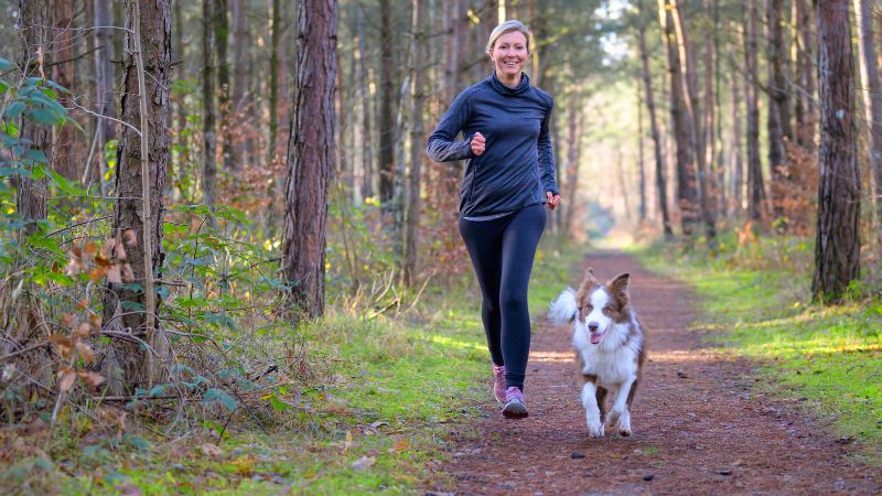 Frau mit Hund beim Joggen im Wald für ihr Selbstwertgefühl